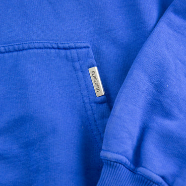 The label of the Represent Owners Club Blue Hoodie.