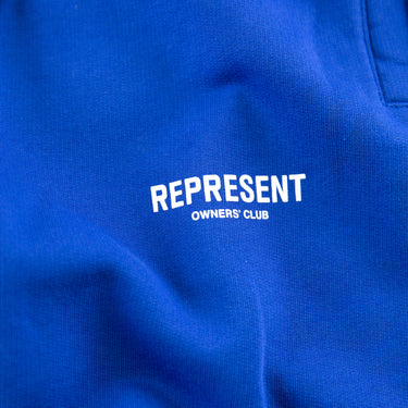 The logo of the Represent Owners Club Blue Sweatpants.